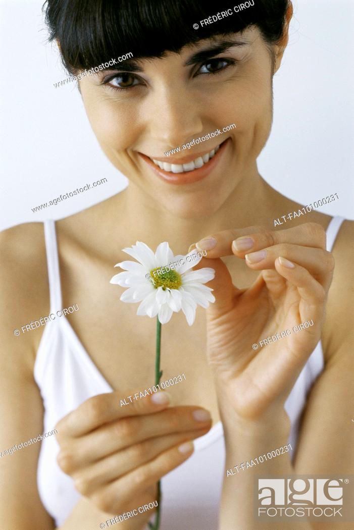 Stock Photo: Young woman plucking petals from flower, smiling, portrait.