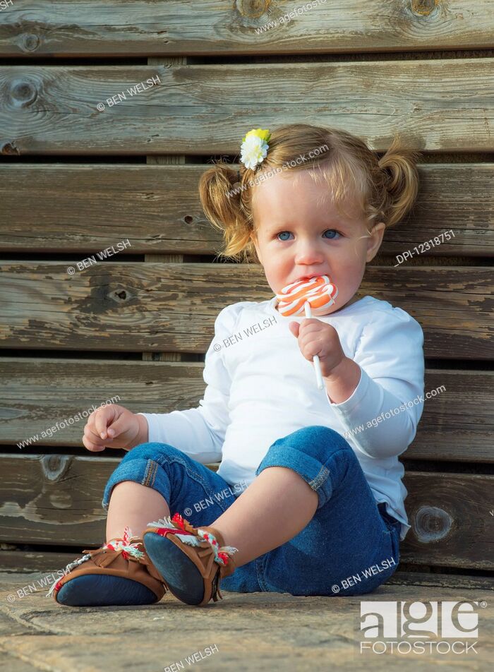 Young girl with blond hair and blue eyes sitting and eating a lollipop;  Tarifa, Cadiz, Andalusia, Stock Photo, Picture And Royalty Free Image. Pic.  DPI-12318751 | agefotostock