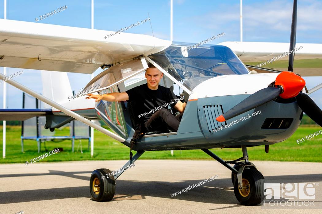 Stock Photo: handsome teenage man sitting in small plane cockpit. young pilot closing door before take off. outdoor shot.