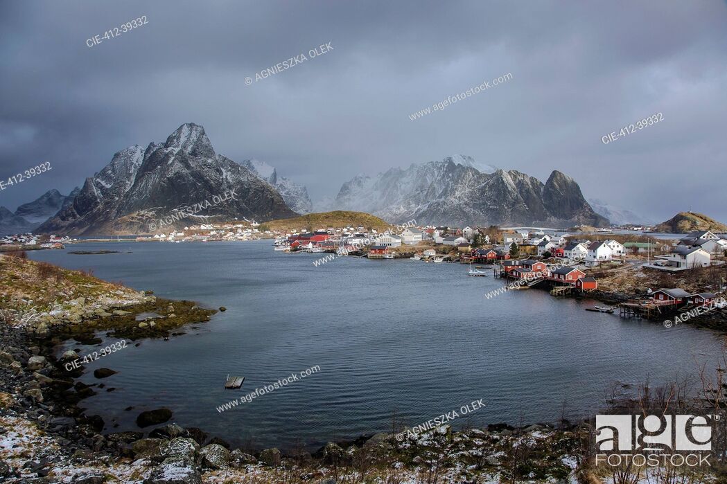 Stock Photo: Fishing village at waterfront below snowy, rugged mountains, Reine, Lofoten, Norway.