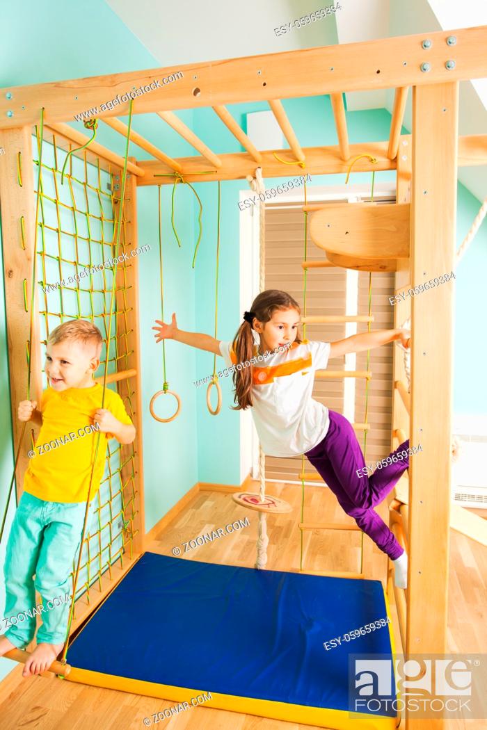 Stock Photo: Happy smiling siblings boy and girl swinging on a wooden ladder and swing on sports complex. Close view of brother and sister happily playing on a kids gym in.