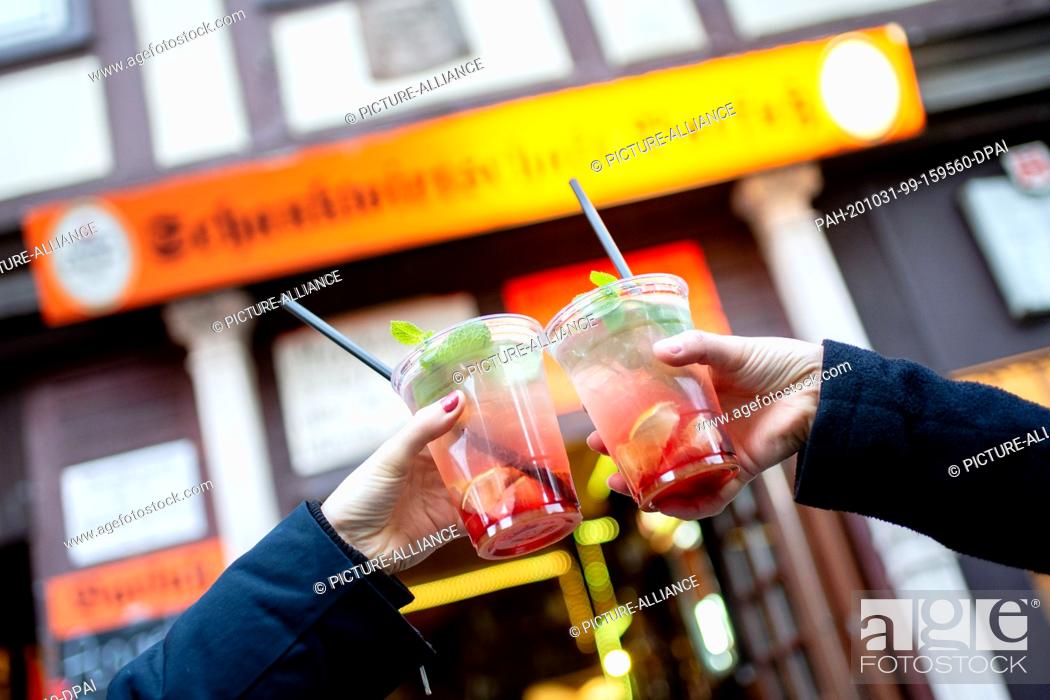 Stock Photo: 31 October 2020, Lower Saxony, Hanover: Two friends toast with a strawberry mojito in front of a bar in the old town. The federal and state governments have.