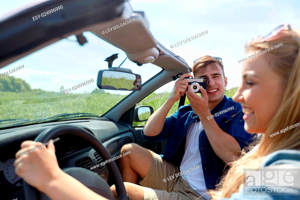 Stock Photo: leisure, road trip, travel and people concept - happy couple driving in cabriolet car and taking picture by film camera.