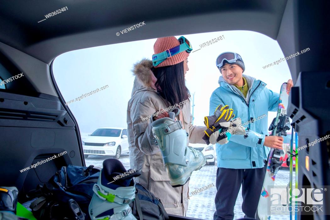 Stock Photo: Parking lot young couples out of the car trunk ski equipment.