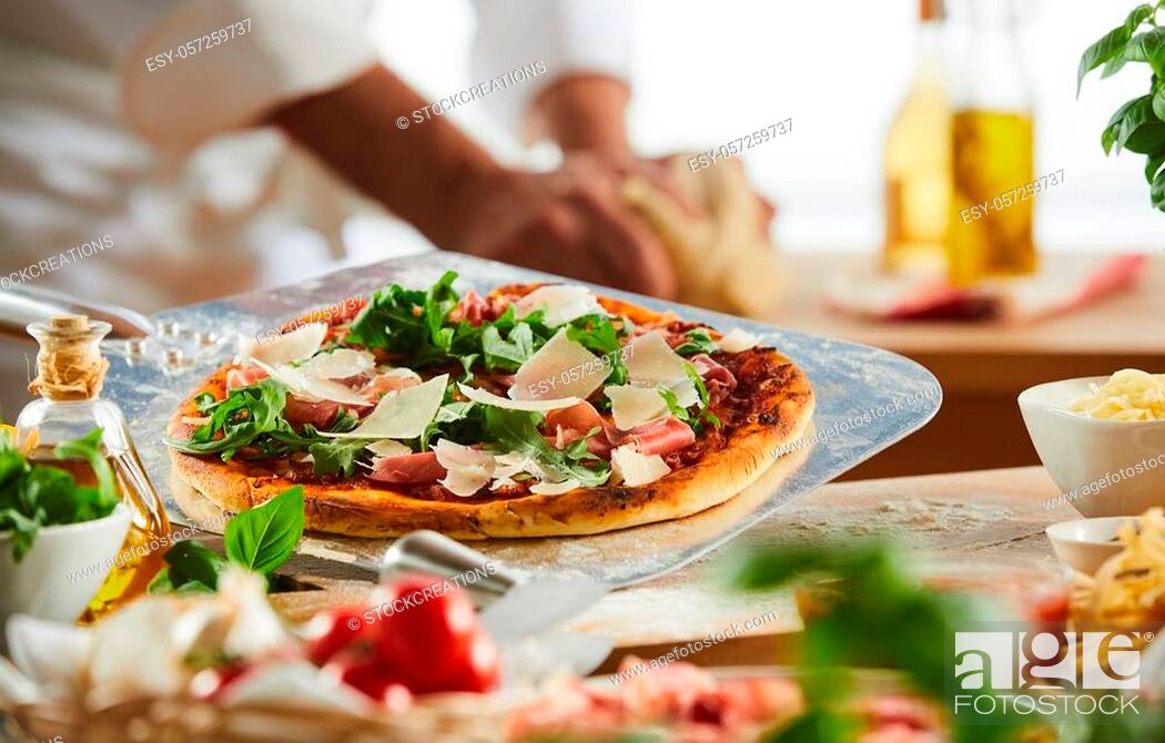Stock Photo: Metal pizzeria paddle with crusty Italian pizza topped with rocket, ham and cheese with foreground ingredients.