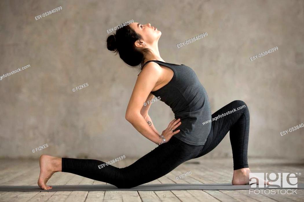 Stock Photo: Young woman practicing yoga, doing Horse rider exercise, anjaneyasana pose, working out, wearing sportswear, black pants and top, indoor full length.