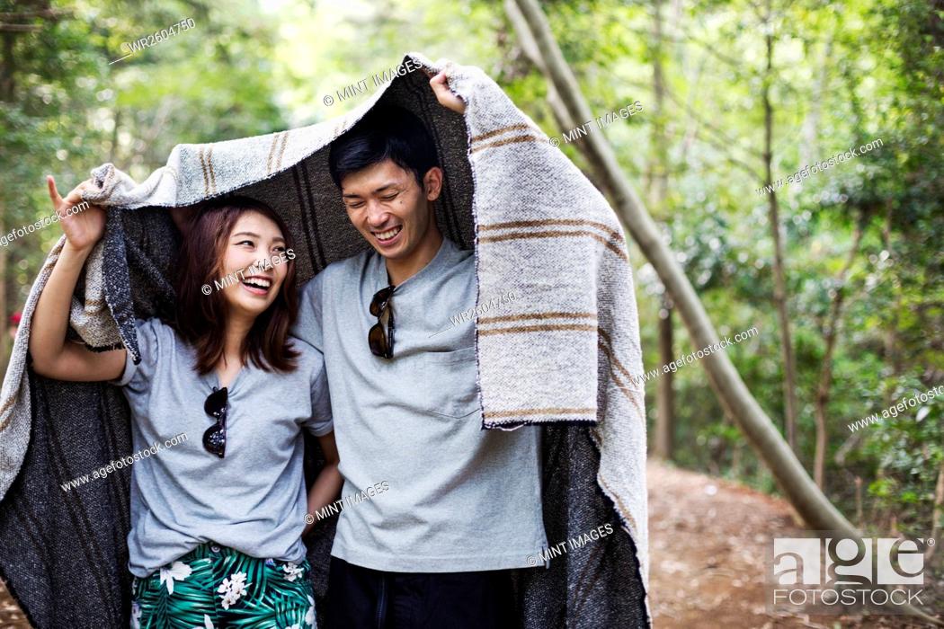 Stock Photo: Young woman and man standing in a forest, holding a blanket over their heads.