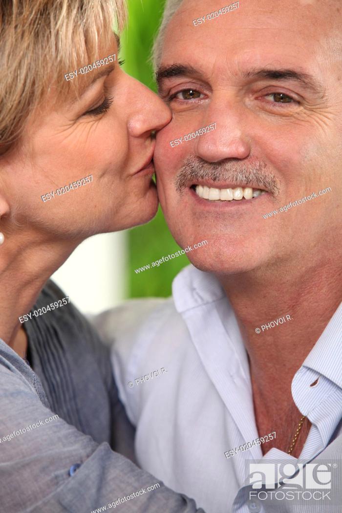 Stock Photo: Mature woman kissing a smiling man on the cheek.