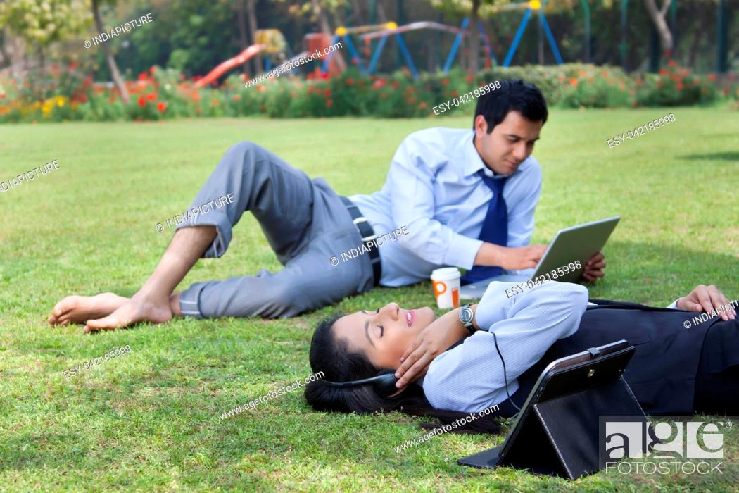 Stock Photo: Businessman working in the park while businesswoman relaxes.