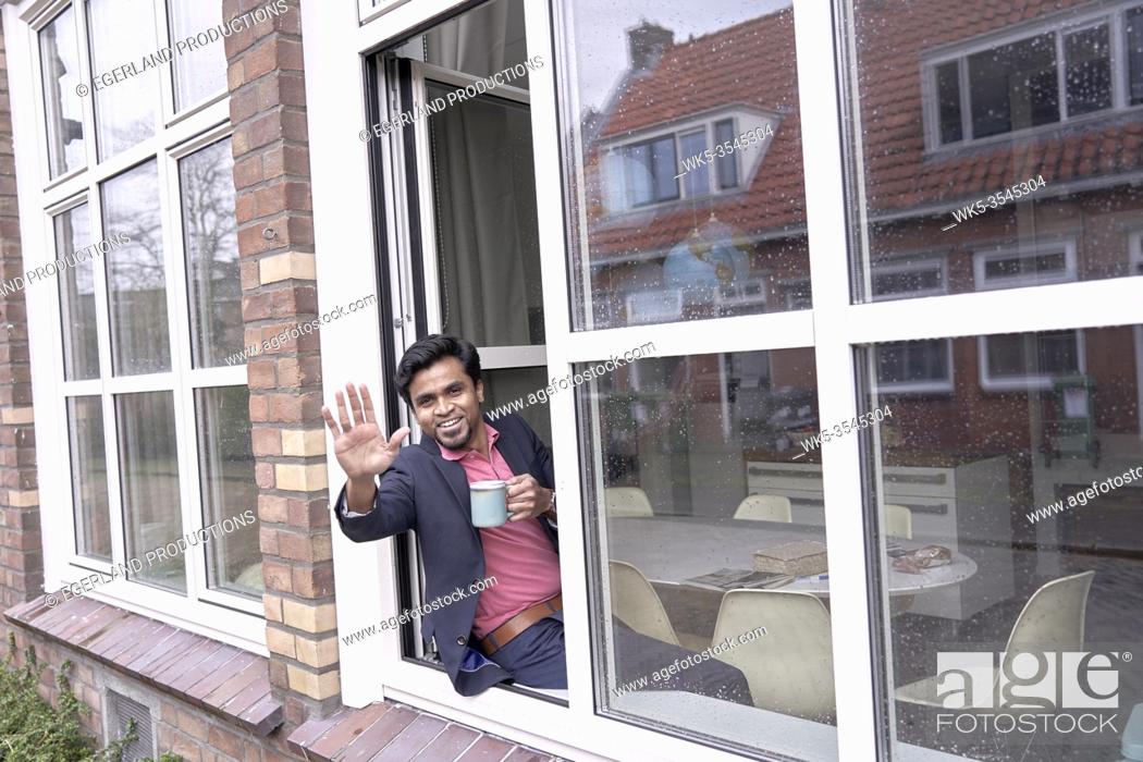 Stock Photo: successful Indian man waving from the window of his modern apartment.