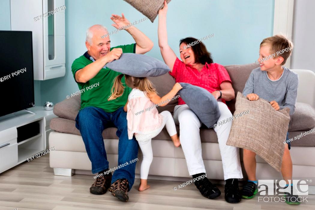 Stock Photo: Grandparent And Kids Having Pillow Fight While Sitting On Couch Together At Home.