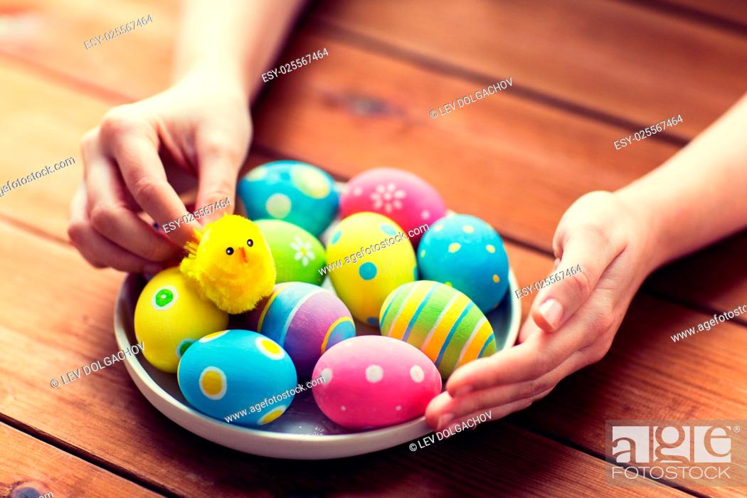 Stock Photo: easter, holidays, tradition and people concept - close up of woman hands with colored easter eggs on plate.