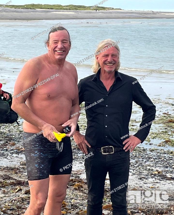 Stock Photo: HANDOUT - 21 August 2021, Schleswig-Holstein, Helgoland: Extreme swimmer Andre Wiersig (l) laughs after arriving ashore in the pig bay of the Helgoland dune.