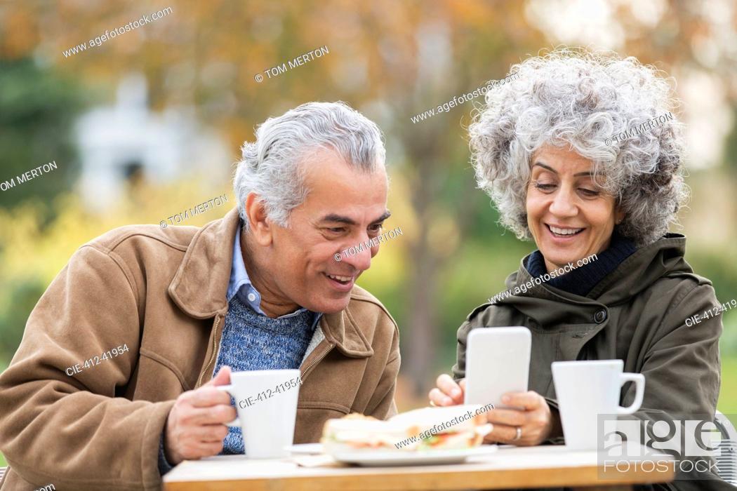 Stock Photo: Senior couple with smart phone, eating lunch and drinking coffee in park.