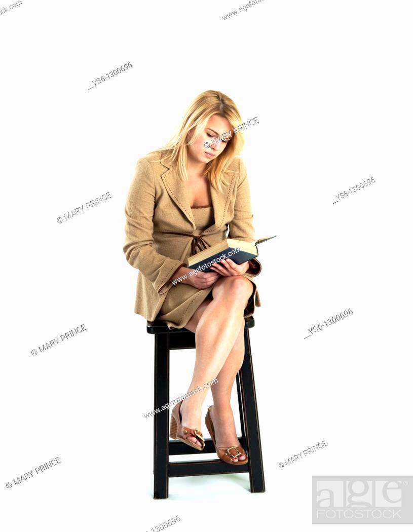 Photo de stock: Young blonde woman in business suit reading a book sitting on a stool.