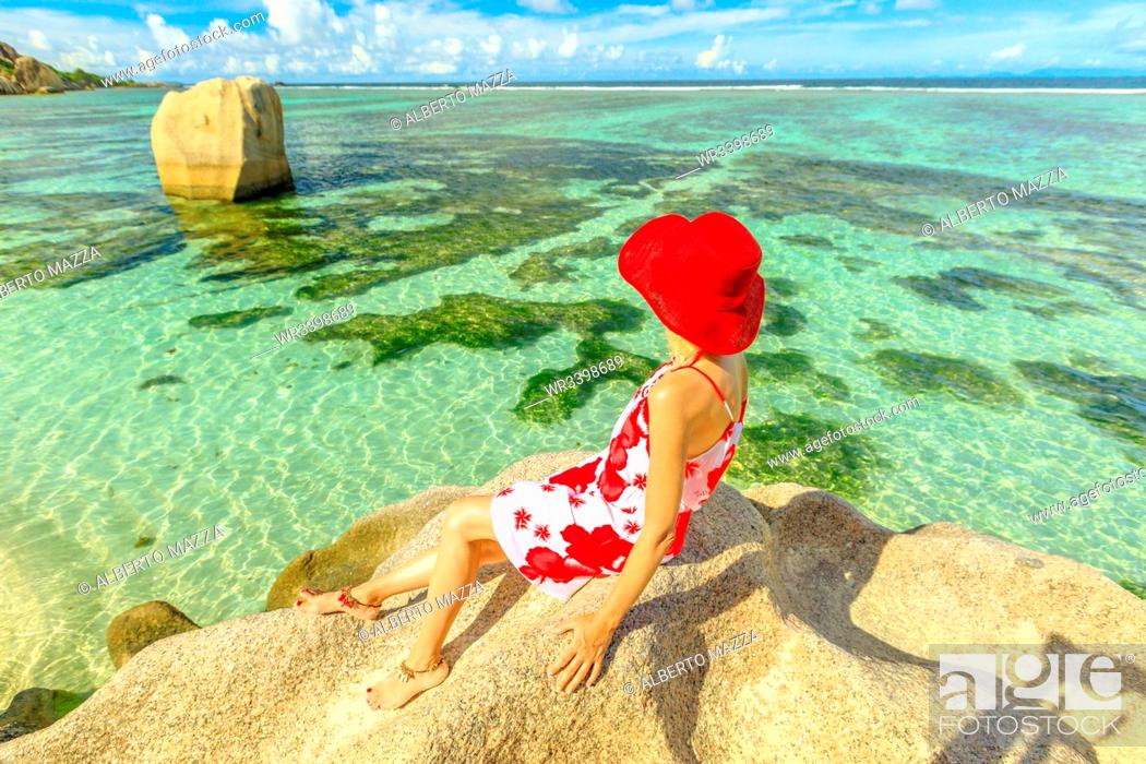 Stock Photo: Tourist woman in red hat on a granite boulder at Anse Source d'Argent, La Digue Island, Seychelles, Indian Ocean, Africa.