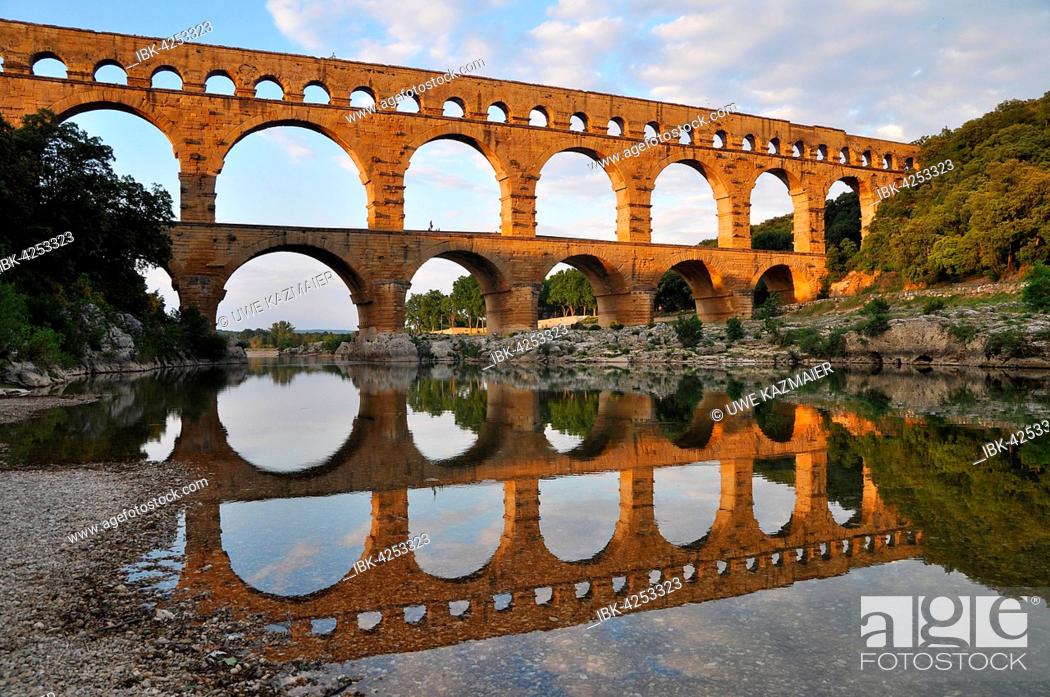 Stock Photo: Roman aqueduct Pont du Gard reflected in the Gardon river in the evening, Remoulins, Provence, Southern France, France, Europe.