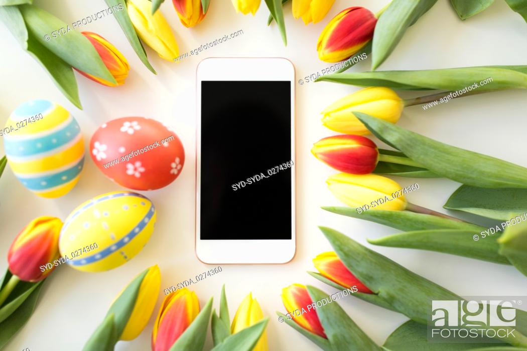 Stock Photo: smartphone with easter eggs and tulip flowers.