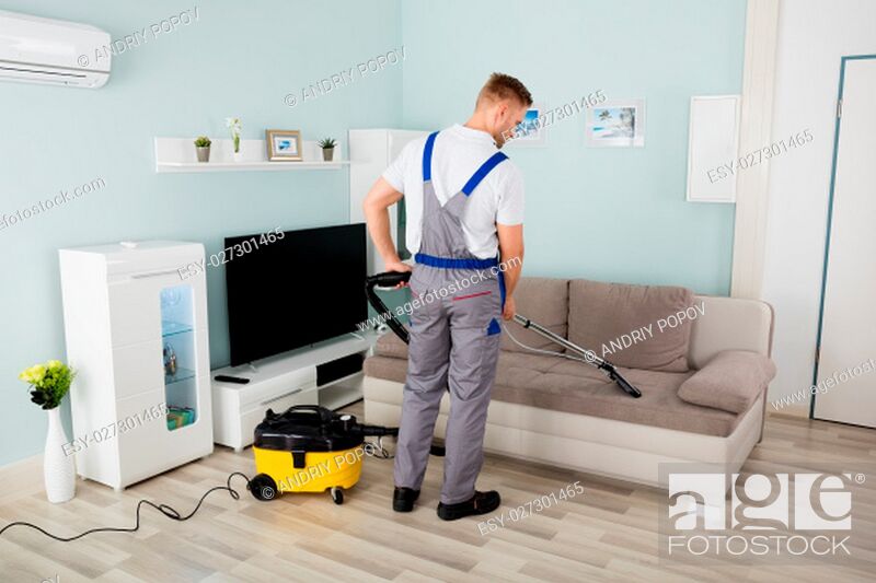 Stock Photo: Rear View Of Young Male Worker Cleaning Sofa With Vacuum Cleaner.