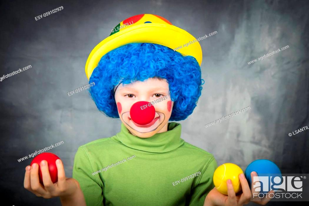 Stock Photo: young child dressed as a clown with wig and fake nose has fun playing with colorful balls celebrating carnival.