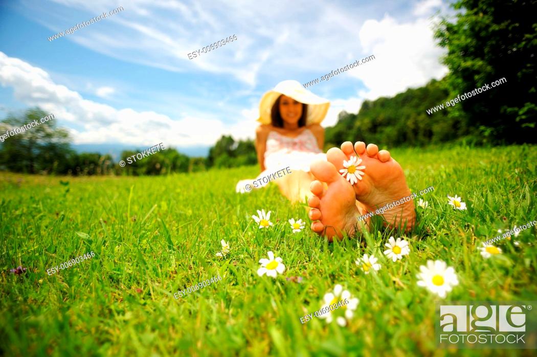 Stock Photo: a smiling young woman is lying on a green lawn, with a daisy between her toes shallow deep of field selective focus DOF.