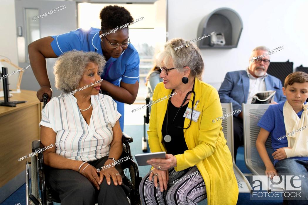 Stock Photo: Female doctor with digital tablet talking to senior patient in wheelchair in clinic lobby.