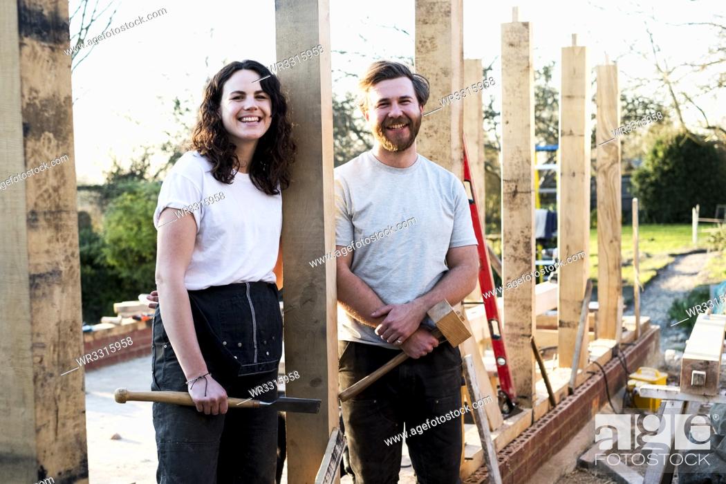 Stock Photo: Smiling man and women holding hand tools standing on building site of residential building.