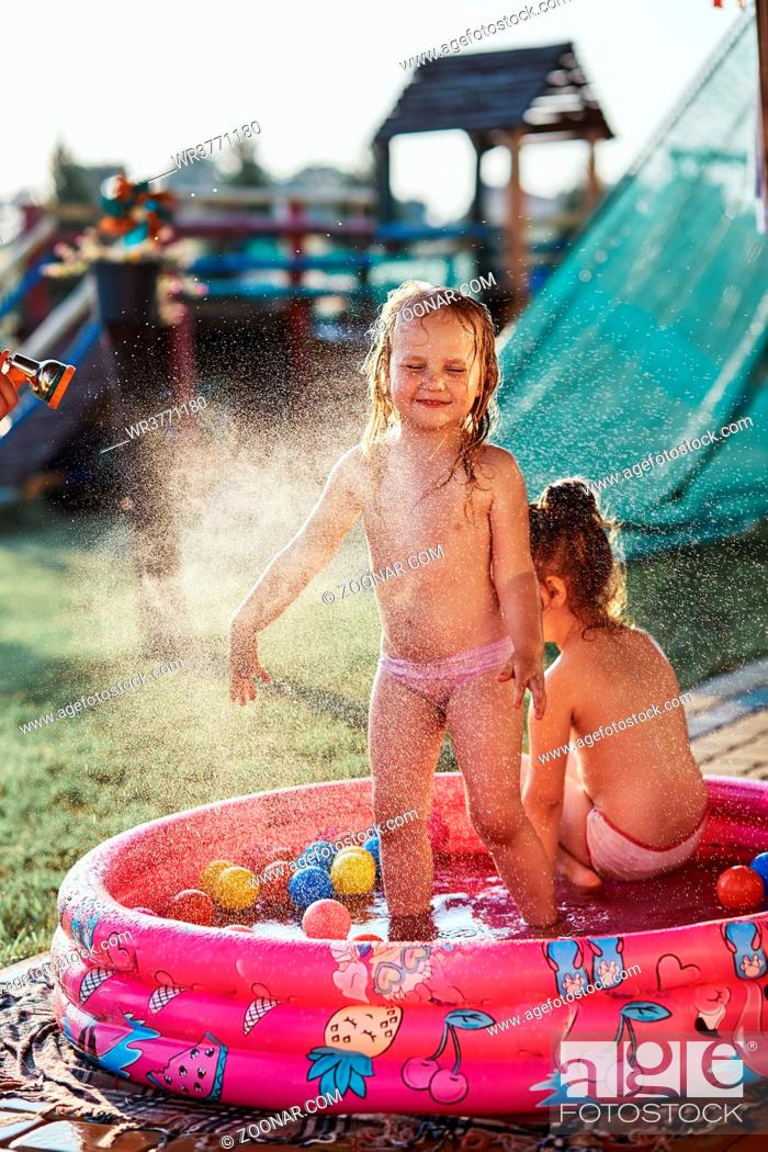 Stock Photo: Little cute adorable girls enjoying a cool water sprayed by their father during hot summer day in backyard. Candid people, real moments, authentic situations.