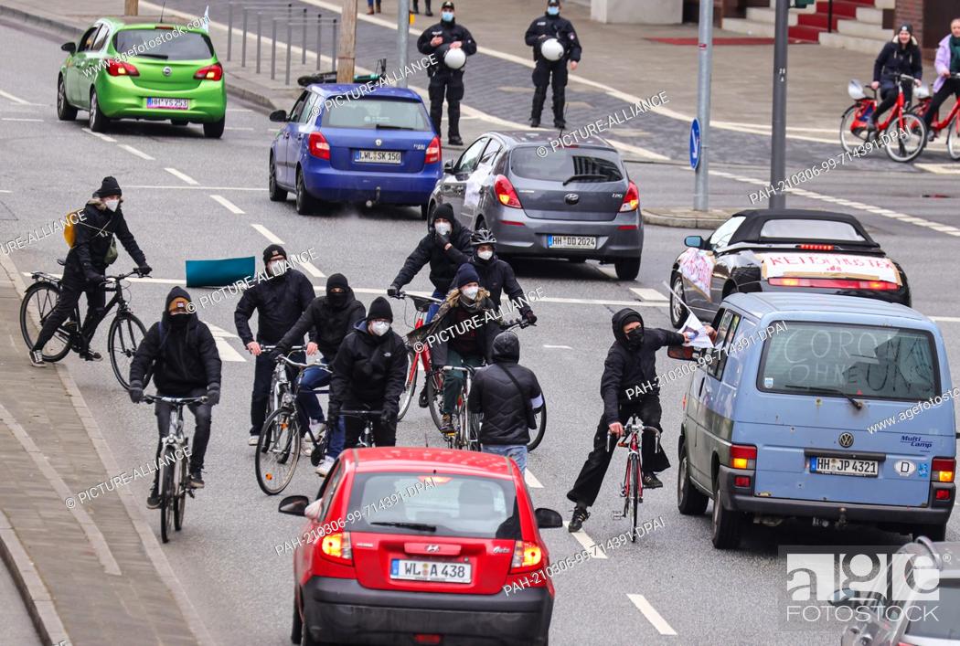 Stock Photo: 06 March 2021, Hamburg: Counter-demonstrators on bicycles tear posters off cars. With the cars people demonstrate against the Corona measures.