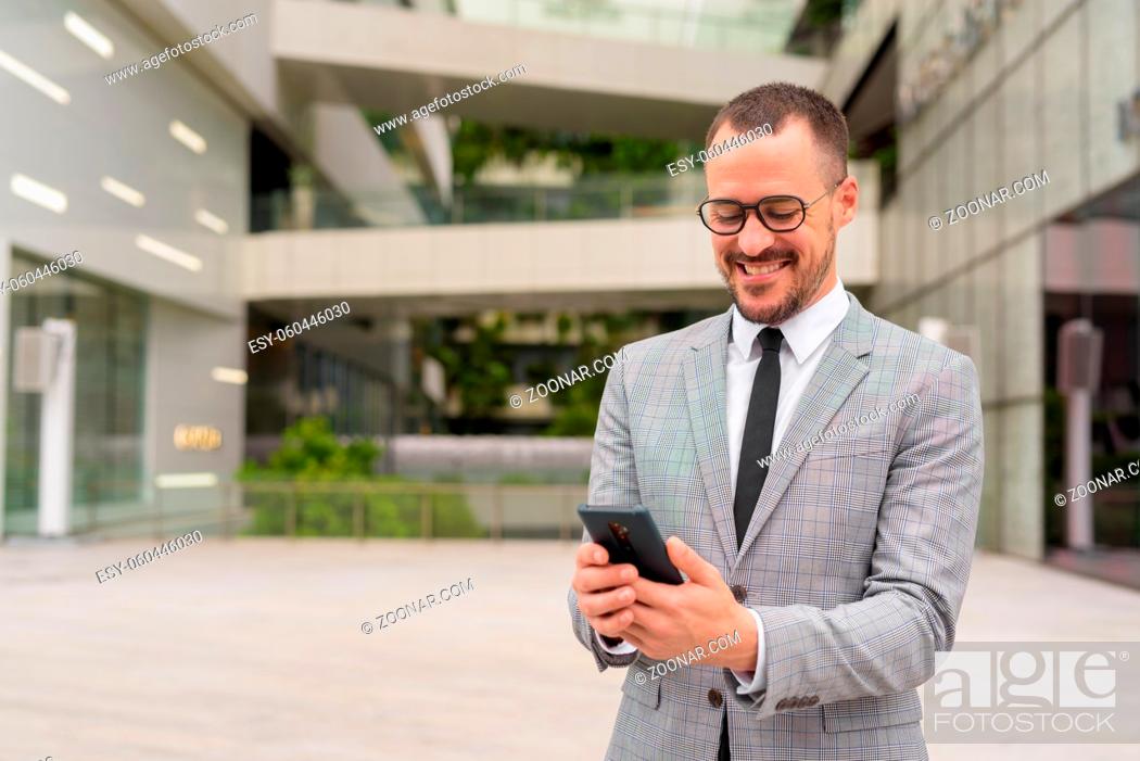 Stock Photo: Portrait of handsome Hispanic bald bearded businessman wearing suit in the city streets outdoors.