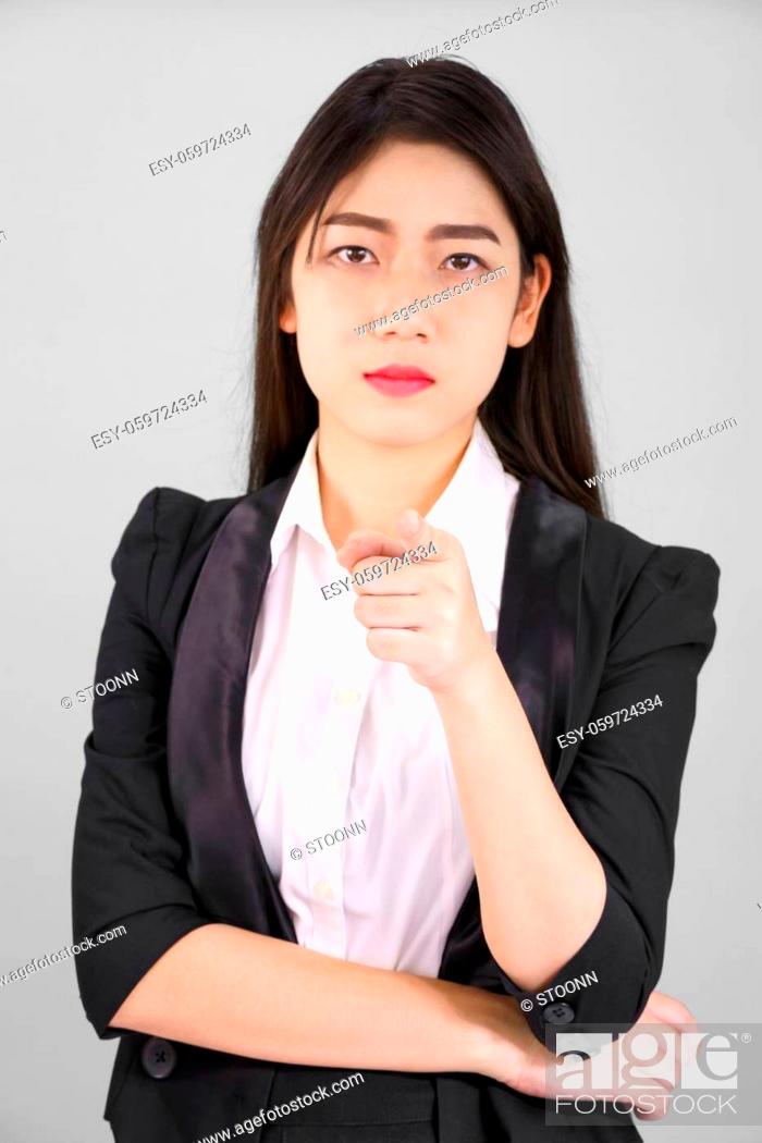 Stock Photo: Asian woman in suit looking at camera and pointing finger on gray background.