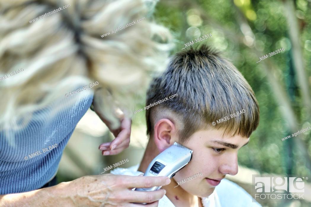 Stock Photo: Portrait of a mother cutting young caucasian boy's hair outside in a garden. Lifestyle concept.