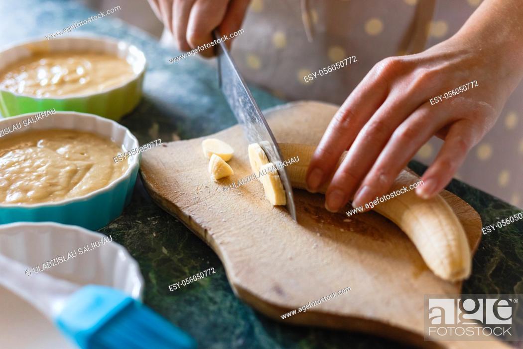 Stock Photo: Woman cuts a banana with a knife on rude wooden board.