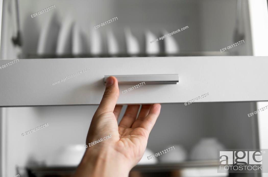 Stock Photo: Hand holds the door of the dryer with utensils. Dish drying metal rack with white clean plates. Traditional comfortable kitchen.