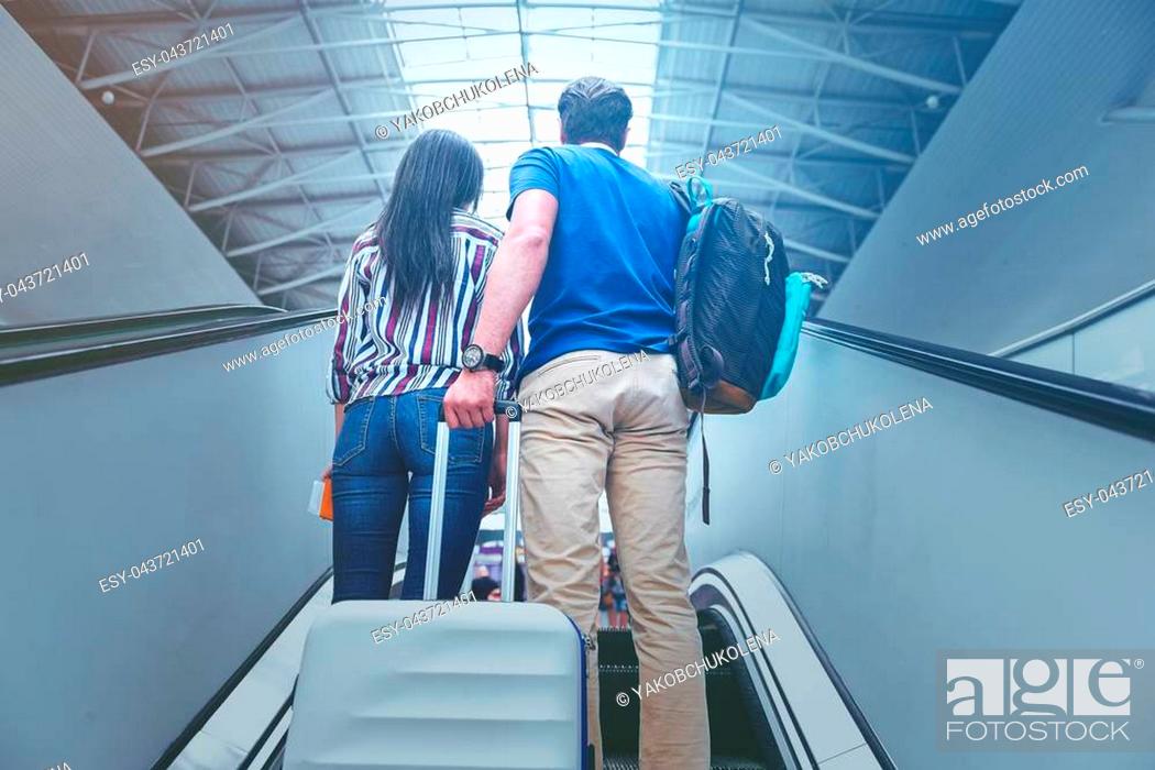 Stock Photo: Happy to travel together. Low angle of young lovers from behind are climbing up on escalator at airport with suitcase.