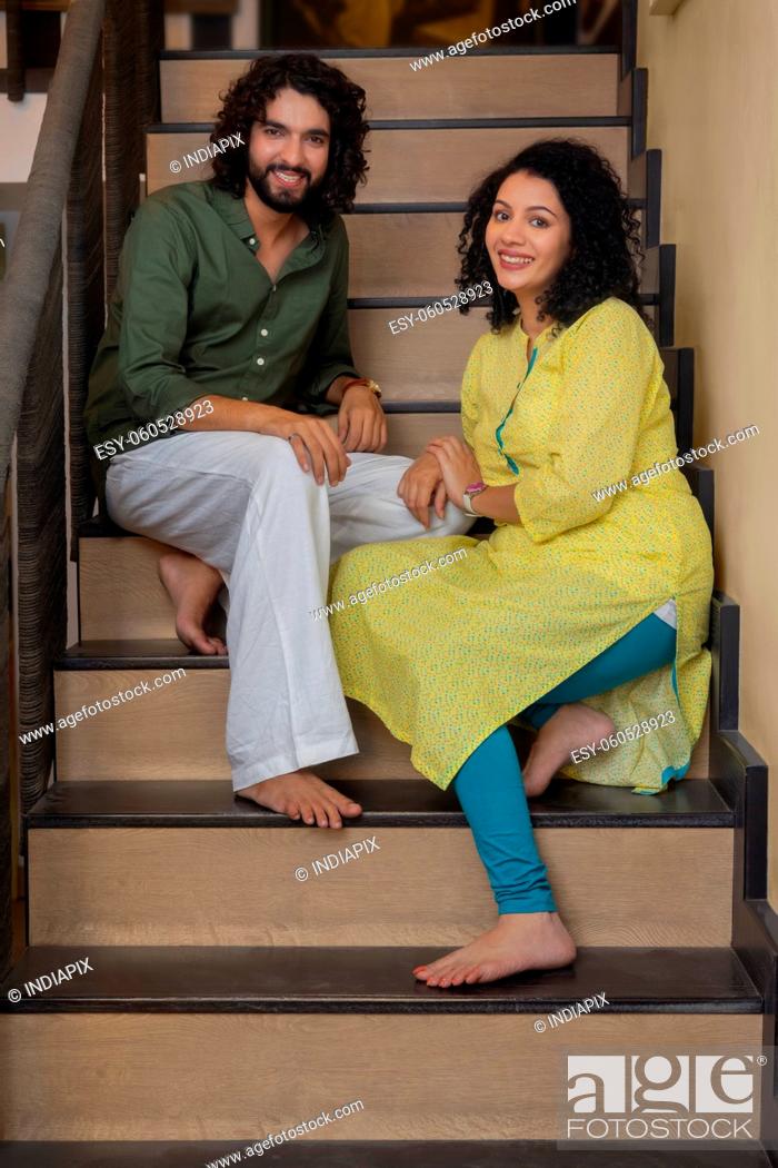Stock Photo: Young couple posing in front of camera while sitting on stairs at home.