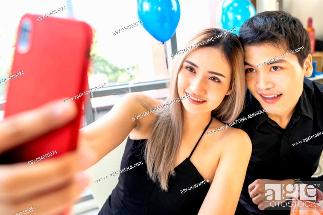 Stock Photo: Young asian adult couple make selfie photographing for celebrating New Year and Christmas holiday together in living room of big apartment in big city.