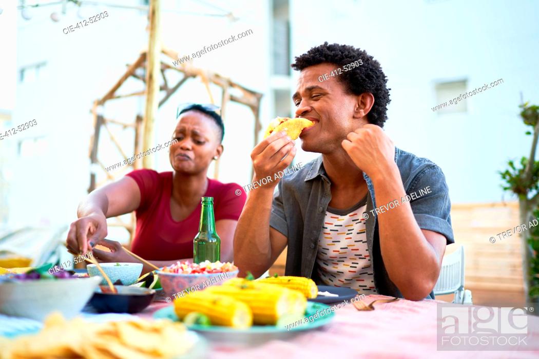 Stock Photo: Young man eating taco lunch at patio table.