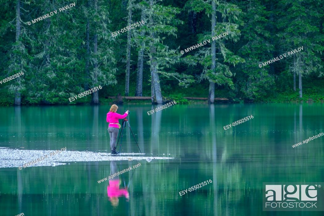 Stock Photo: Germany. Calm forest lake in a dense forest. Girl photographer stands on the edge of the water and makes photos with a tripod.