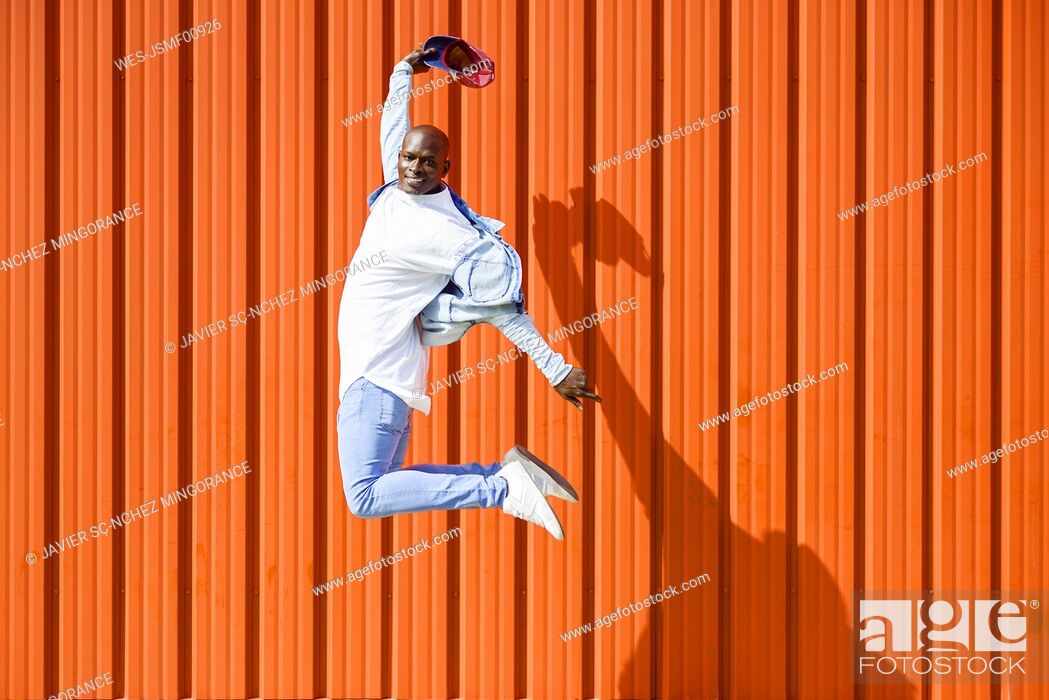 Stock Photo: Man wearing casual denim clothes jumping in the air in front of orange wall.