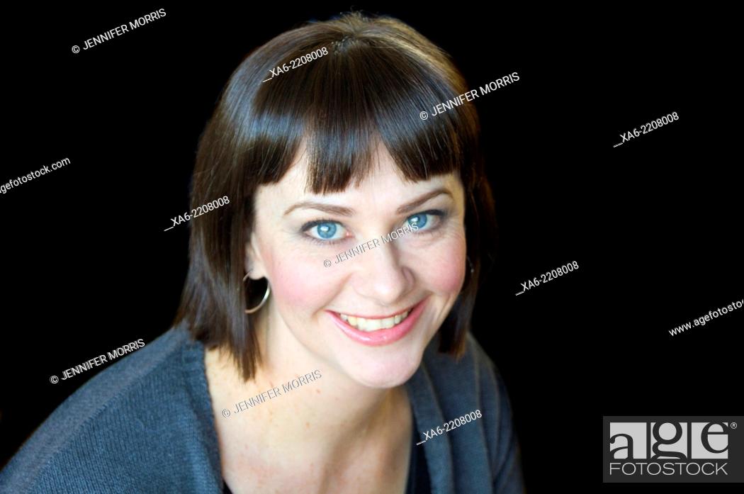 Stock Photo: A 30-something woman smiles at the camera against a black background.