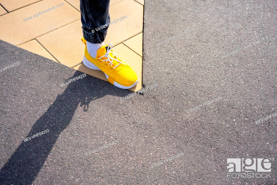 Stock Photo: Boy wearing yellow shoe while standing on footpath.