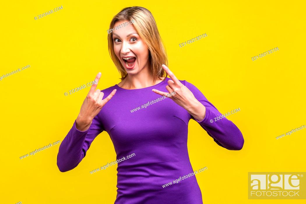 Stock Photo: Portrait of crazy funny woman in elegant purple dress looking at camera with excited happy face and showing rock symbol with fingers up, devil horns.