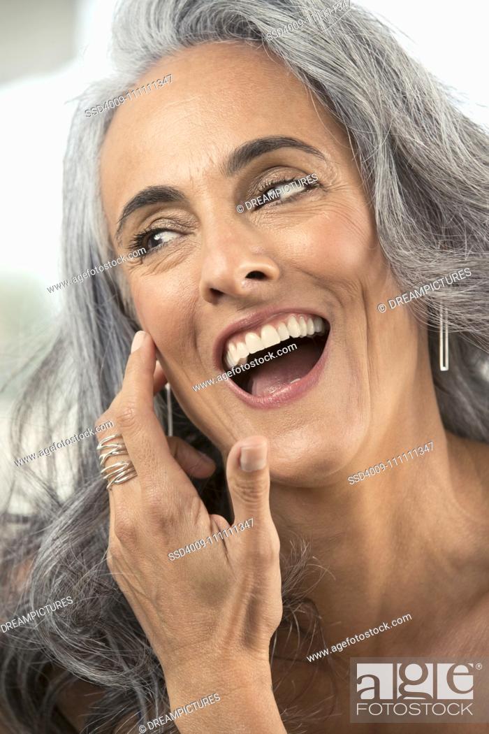 Stock Photo: Middle-aged woman with gray hair brushes hair out of her face and looks off camera laughing.