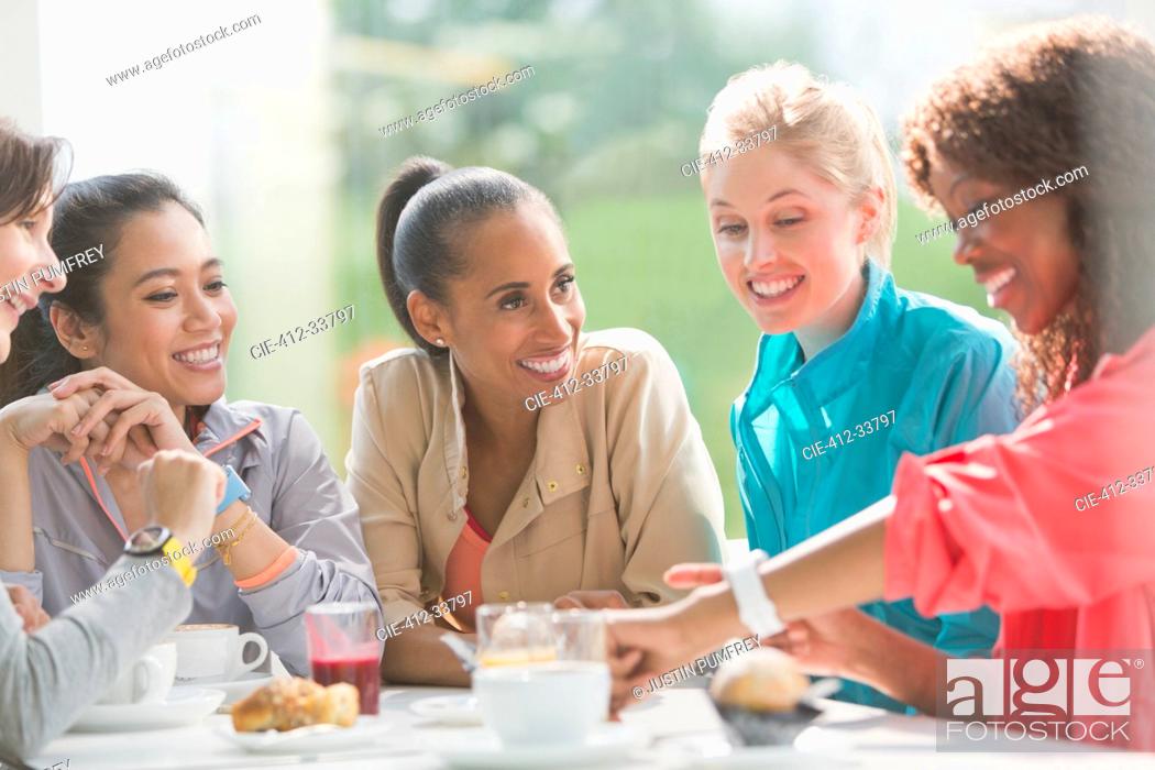 Stock Photo: Women talking and looking at smart watch at cafe table post workout.