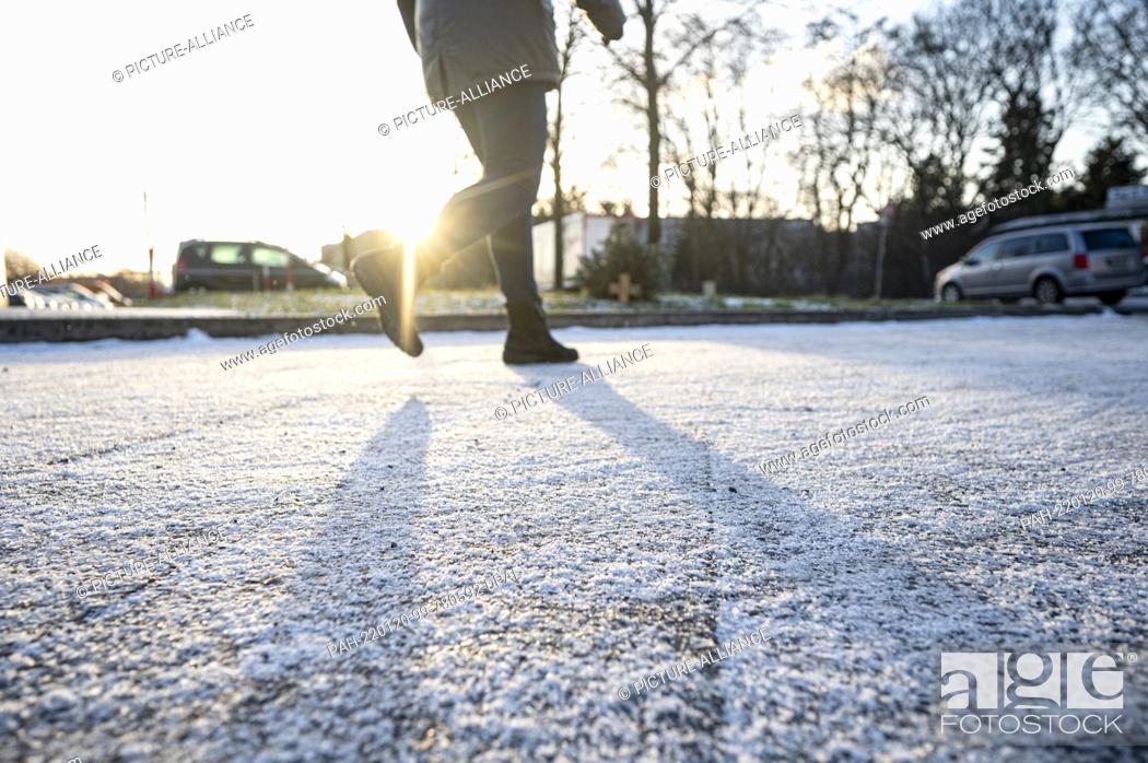Stock Photo: 20 January 2022, Berlin: A walker walks over a thin layer of snow on a sidewalk in Berlin's Prenzlauer Berg neighborhood in the morning.
