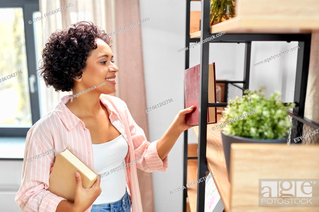 Stock Photo: smiling woman arranging books on shelving at home.