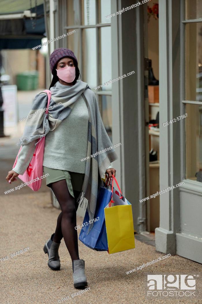 Stock Photo: Young woman in face mask with shopping bags on sidewalk.