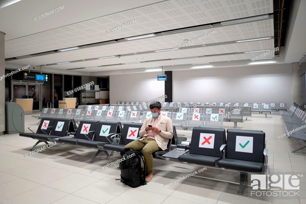 Stock Photo: Traveler sits at international airport of Cyprus, Paphos during COVID-19 crisis, sits in terminal on seat with social distance markings wearing mask.