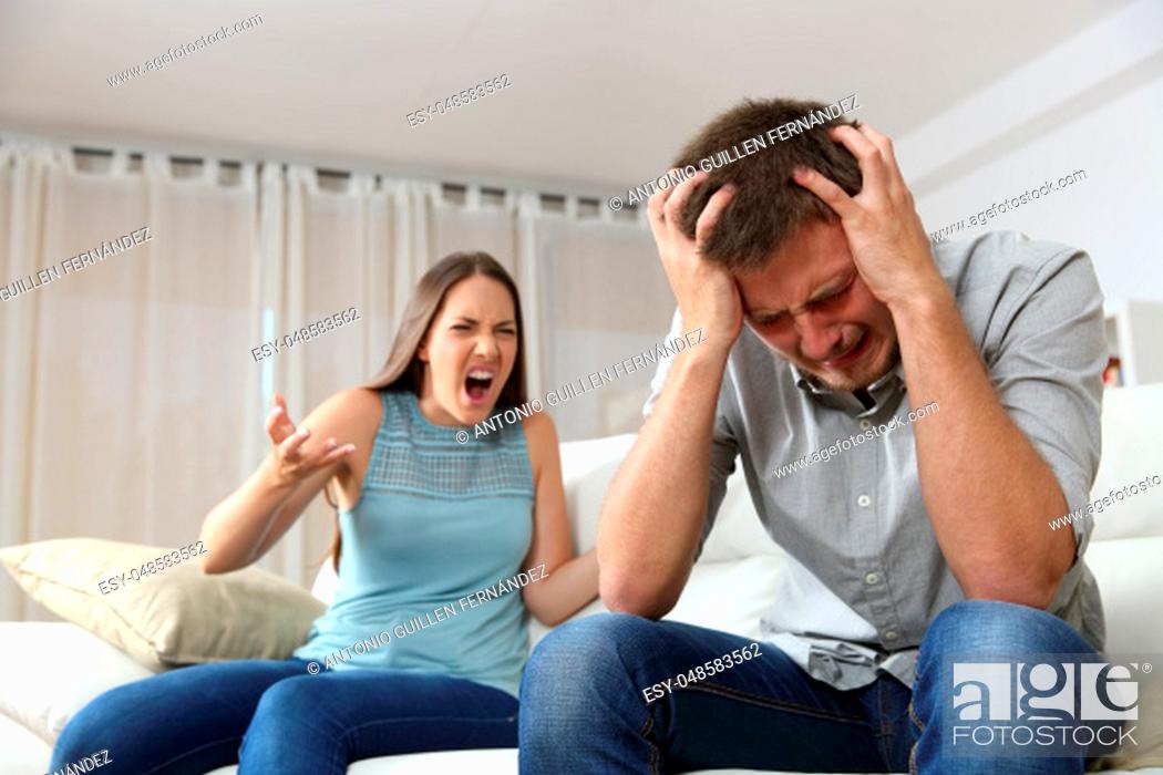 Stock Photo: Couple arguing. Wife shouting to her desperate husband sitting on a couch in the living room at home.
